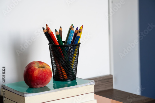 Canvastavla Stack of books with red apple and colored pencils in holder on wooden desk for e
