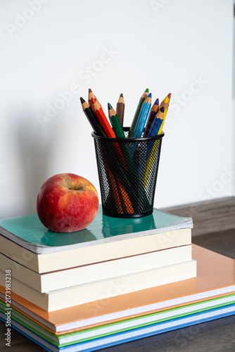 Stack of books with red apple and colored pencils in holder on wooden desk for education concept