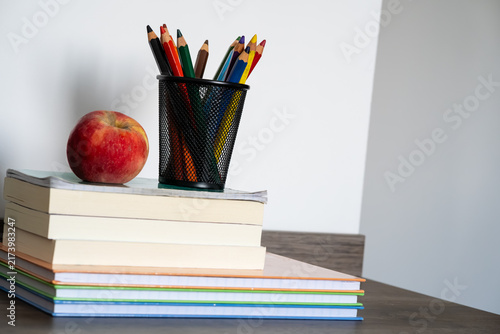 Fotografie Stack of books with red apple and colored pencils in holder on wooden desk for e