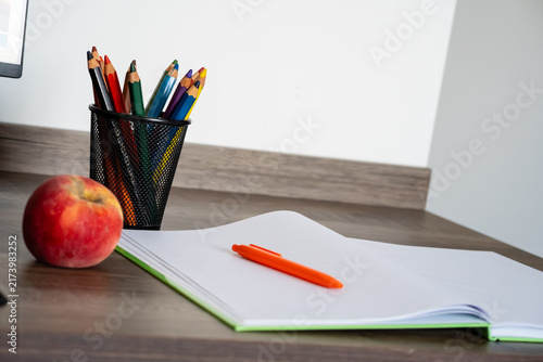 Quadro su tela Open blank notebook with orange pen, colored pencils, and red apple on wooden de