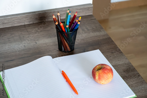 Bild auf Leinwand Open blank notebook with orange pen, colored pencils, and red apple on wooden de