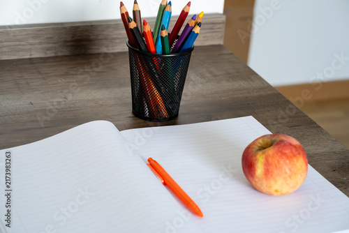 Konstfotografi Open blank notebook with orange pen, colored pencils, and red apple on wooden de