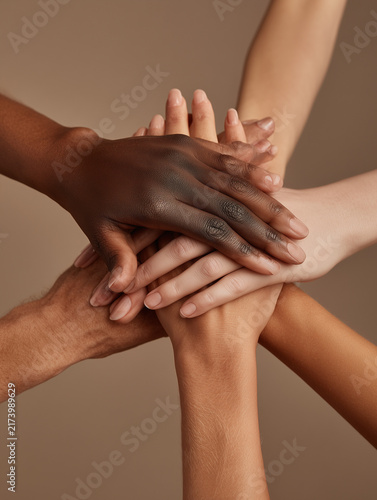 A photo of six hands from different ethnicities placed on top of each other, symbolizing unity and diversity.