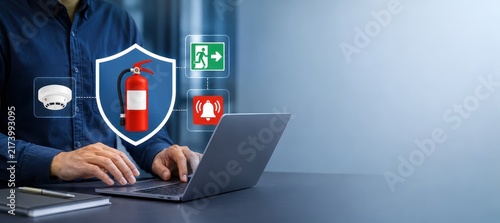 Digital Fire Safety Protocol: A person's hands operate a laptop displaying icons of fire safety equipment such as a fire extinguisher and smoke detector, symbolizing advanced protection systems.