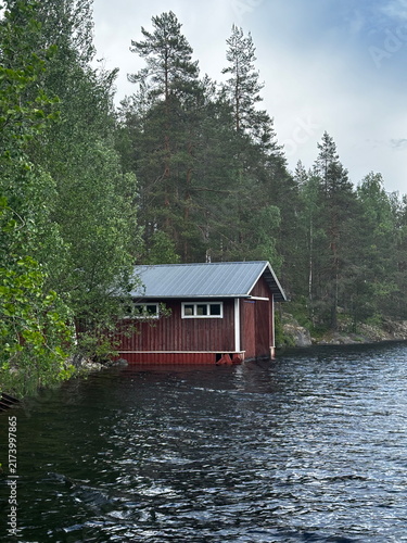 Foto Red fishing boathouse on Finnish lake with forest and rocks, summer day