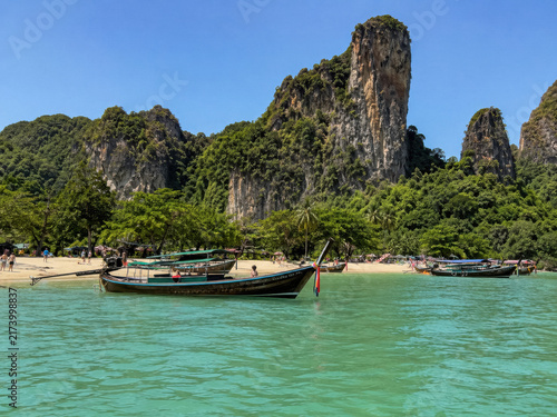 Long tail boats floating in clear emerald water beneath limestone cliffs on a Thai island beach.generative AI