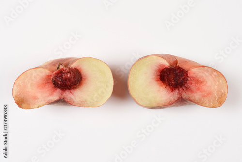 Cuadro en lienzo A high angle side view of a ripe flat saturn peach cut into two halves showing its inner stone and white flesh on a plain white surface