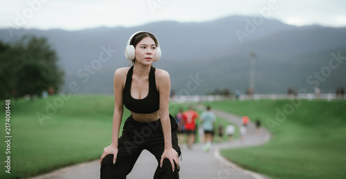 Young woman wearing black activewear and headphones, stretching her arms outdoors on a green grassy field, enjoying a healthy and relaxing fitness lifestyle.
