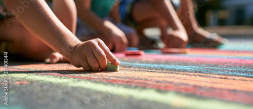 Children drawing with colorful chalk on pavement in bright daylight  