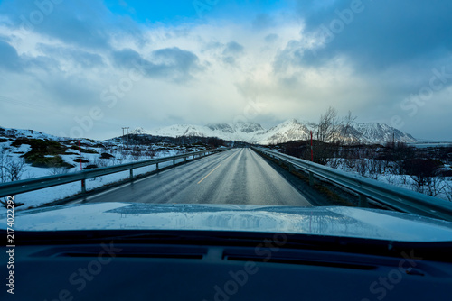 Beautiful scenic winter landscape of an empty asphalt road winding past majestic snow-covered mountains and a frozen fjord in Lofoten, Norway. Concept of adventure and freedom on an Arctic Scandinavia