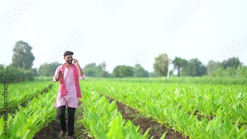 young indian farmer talking on mobile phone at green turmeric agriculture field