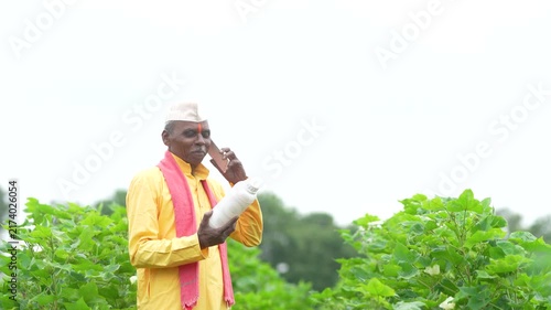Senior indian farmer holding pesticide bottle at agriculture field and talking on mobile phone 