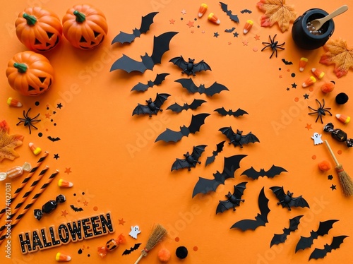 Vibrant Halloween flat lay on orange background with many black paper bats decorative pumpkins candy corn plastic spiders autumn leaves and festive confetti for spooky season celebration