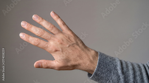 Human hand raised in a waving goodbye gesture with open fingers against a clean gray background, representing greeting, farewell, communication and social interaction.