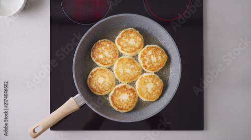 Traditional syrniki pancakes frying in a stone pan on induction stove