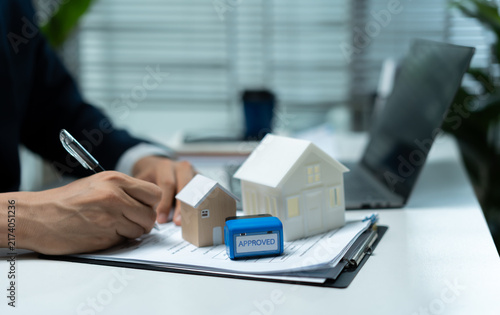 Фотография Real estate businessman reviewing approved property documents with house models and laptop, representing mortgage approval, home financing, loan application and property purchase process