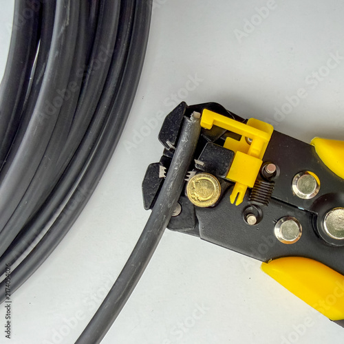 Canvastavla Yellow automatic wire stripper tool cutting a thick black electric wire close up