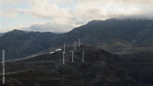Wind turbines generating clean renewable energy on the dramatic coastal mountain cliffs of Madeira under soft overcast sky light for sustainability concept. 4K video.
