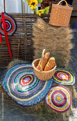 Crocheted mats and a woven basket with bread are arranged on a hay bale in a rustic market setting