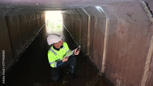 Worker Using Flashlight to Inspect Water Flow Inside Concrete Drainage Tunnel