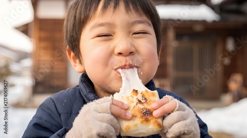 Naklejka 冬の屋外で伸びるお餅を夢中で頬張る男の子