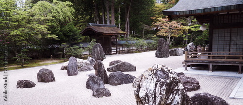 Foto 日本の寺院にある静寂な枯山水庭園。白砂に描かれた波紋と配置された奇岩、背景の木々と伝統的な木造建築が調和した、静謐で精神的な禅の空間。