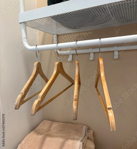 White metal wall rack with a hanging bar holding wooden clothes hangers, and folded towels placed on a shelf below in an organized room
