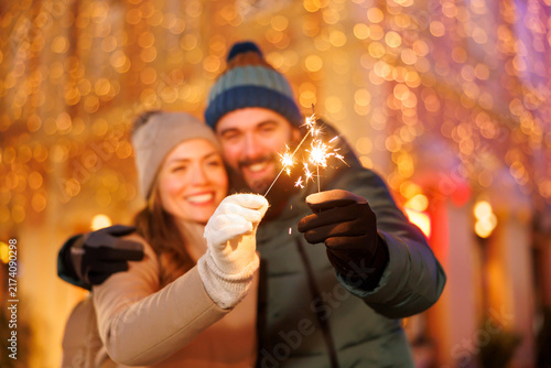 Couple hugging, waving with sparklers and dancing while celebrating New Year in the city square