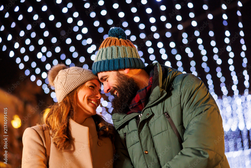 Obraz premium Couple hugging and walking down decorated city streets at Christmas