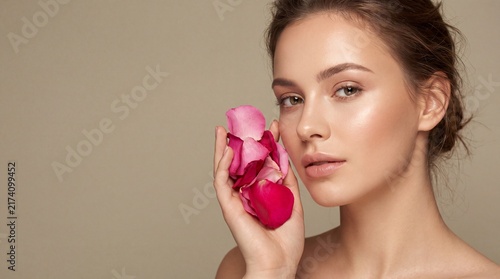 Portrait of young woman holding pink rose petals near face with against beige background close portrait close