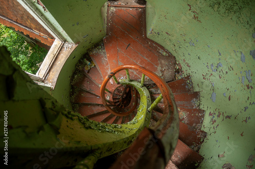 Abandoned overgrown mansion with spiral staircase, old car and ruined interior