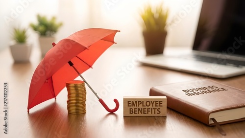 A red umbrella covers a stack of gold coins next to a notebook labeled Business Insurance and a wooden block with EMPLOYEE BENEFITS written on it.