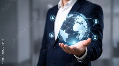 Businessman in a dark navy suit holds a glowing holographic world globe representing global networking connections and digital communication technology