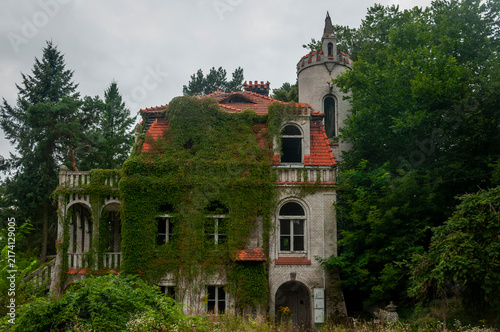 Abandoned overgrown mansion with spiral staircase, old car and ruined interior