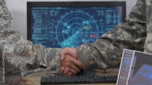 Military personnel shaking hands in control room with tactical radar display screen in background