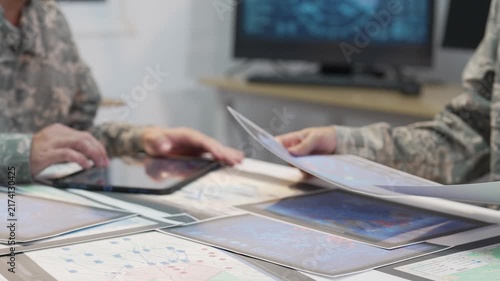 Military officers analyzing tactical map documents and digital tablet in command war room