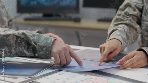 Military officers analyzing tactical map documents and digital tablet in command war room