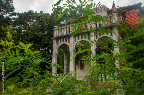 Abandoned overgrown mansion with spiral staircase, old car and ruined interior