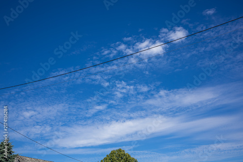Expansive Blue Sky with Delicate White Cloud Patterns. An expansive blue sky photographed through the window of a moving vehicle, filled with thin, elongated white clouds and delicate wispy formations