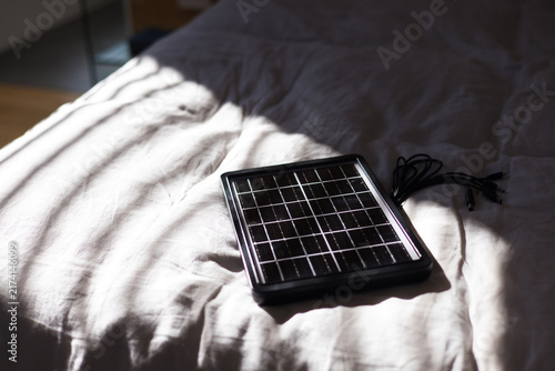 Solar panel is lying on bedding, blinds are casting striped shadows and cables are lying coiled