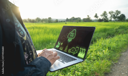 Person using laptop with eco friendly graphics in lush green field, symbolizing sustainable technology