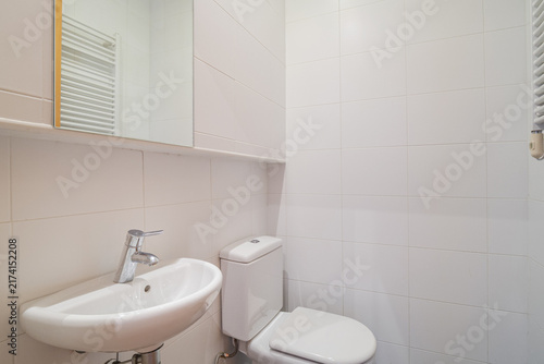 Bright modern bathroom with white toilet wall-mounted sink and mirrored cabinet in tiled interior