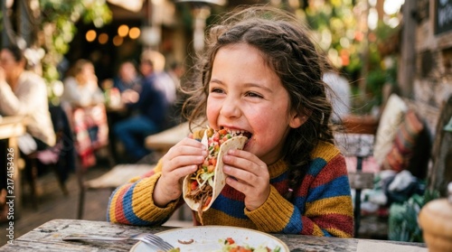 Young girl happily eating a taco at an outdoor restaurant patio.