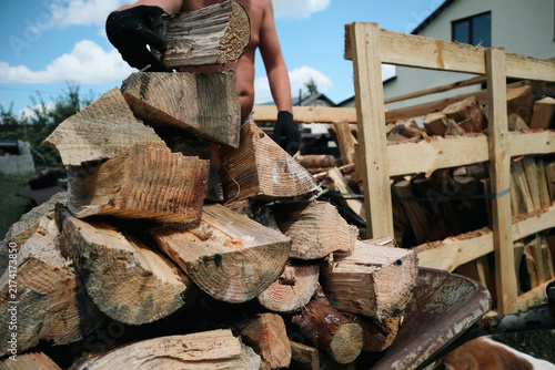 Obraz na płótnie Man wearing protective gloves stacking split wooden logs onto rack preparing fir