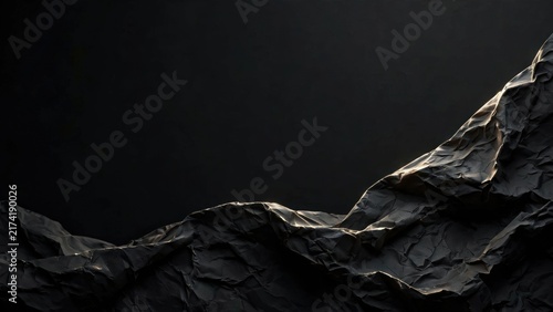 Abstract textured dark surface with dramatic lighting, resembling crumpled paper or rocky terrain