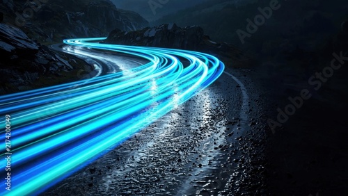 Light trails illuminate a wet, winding road through a dark, mountainous landscape. Speed