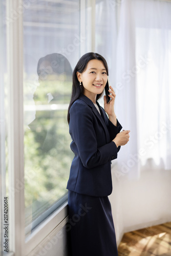 Young Japanese businesswoman talking on a smartphone by a bright window