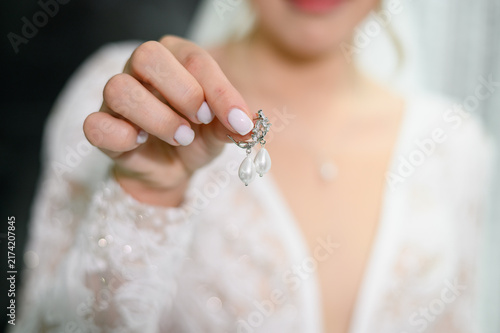 Foto Close up of bride holding beautiful silver earrings with white teardrop pearls,