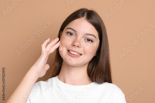 Bild auf Leinwand Beautiful teenage girl with freckles applying cream onto her face against light
