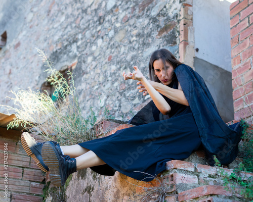Tapety artystyczne Woman in Dark Dress Posing on Weathered Brick Wall